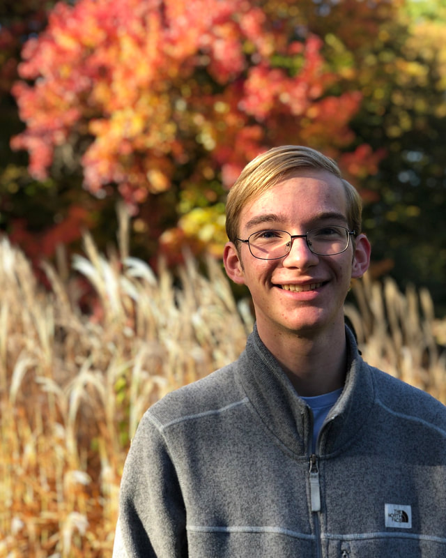 Peter Covert poses outdoors in front of a grassy field and trees.