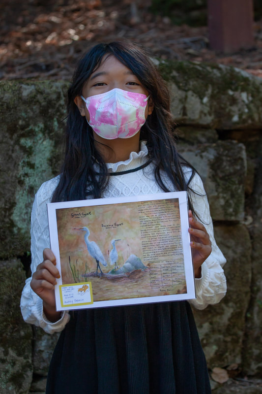 A young girl holding up her bird artwork